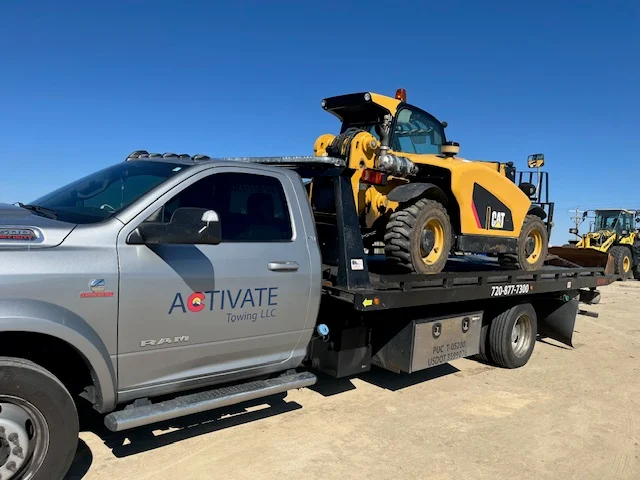Activate Towing flatbed hauling a CAT skid steer — heavy equipment transport across the Front Range