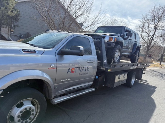 Activate Towing flatbed hauling a Hummer H3 from a neighborhood driveway in Elizabeth, CO